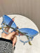 Blue butterfly-shaped sunglasses with gold accents held by a hand against a neutral background