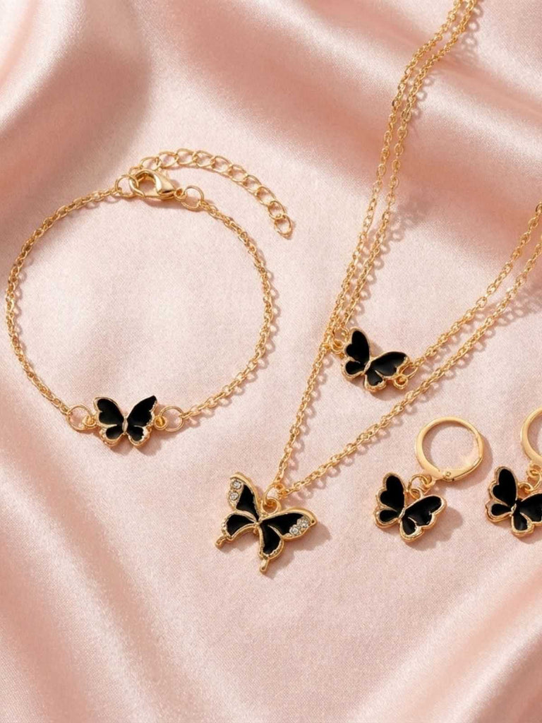 Gold jewelry set with red butterfly charms on a pink fabric background