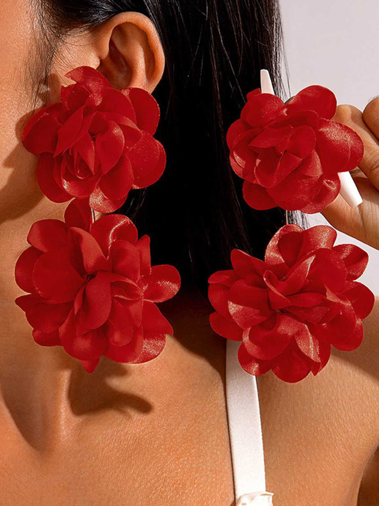 Un mannequin portant de grandes boucles d'oreilles en tissu rouge vif ornées d'un groupe de quatre pétales floraux en 3D pour un effet spectaculaire.